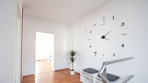 A modern interior with a wooden floor, a white wall clock, a potted plant, and a staircase with a metal railing.