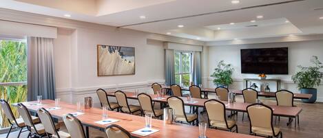 A conference room with multiple tables and chairs, a large painting on the wall, and a television screen.