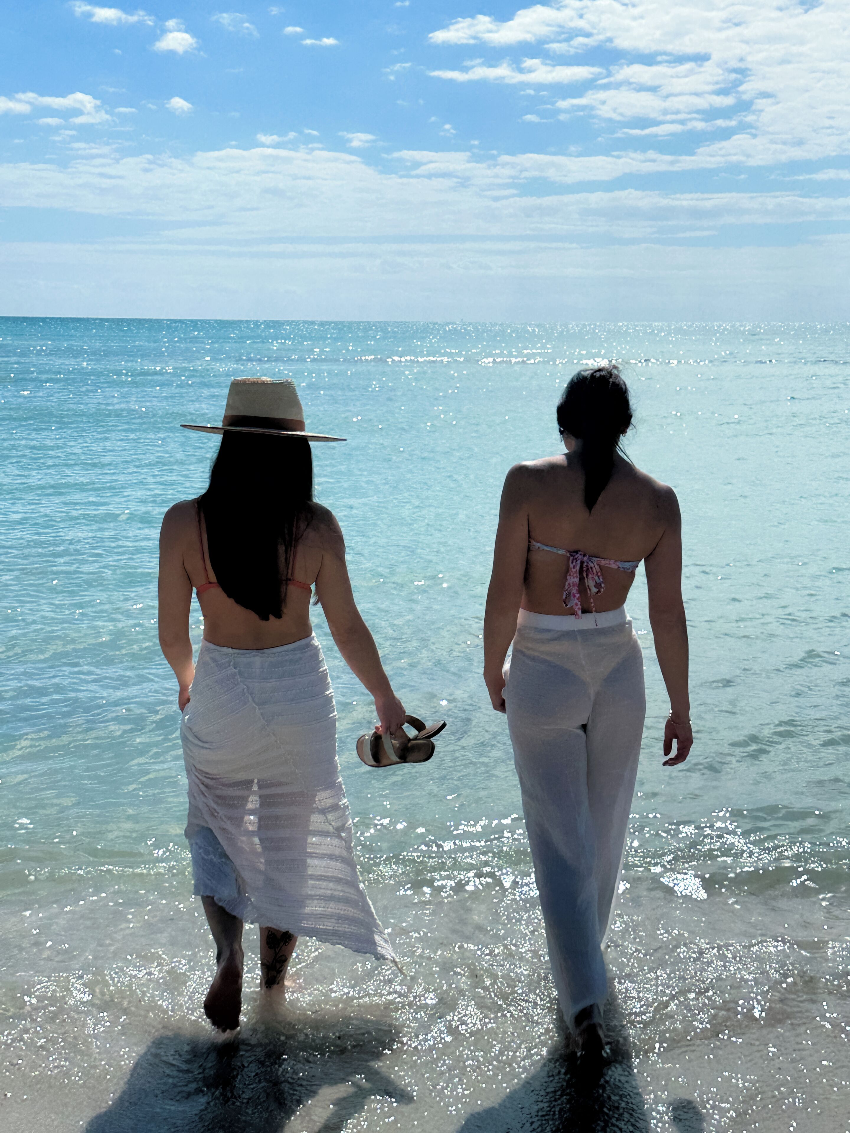 Two people walking on a beach with clear water and a blue sky.