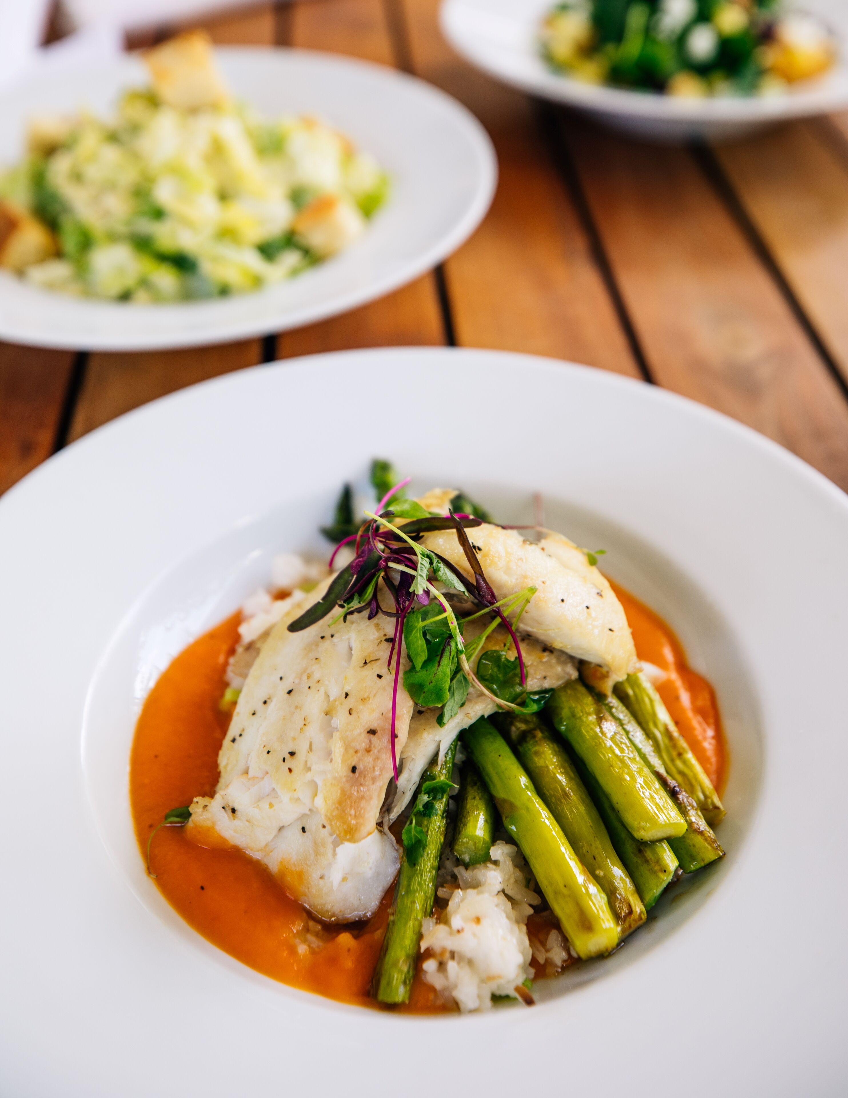 A white plate with a fish fillet, asparagus, and a red sauce.