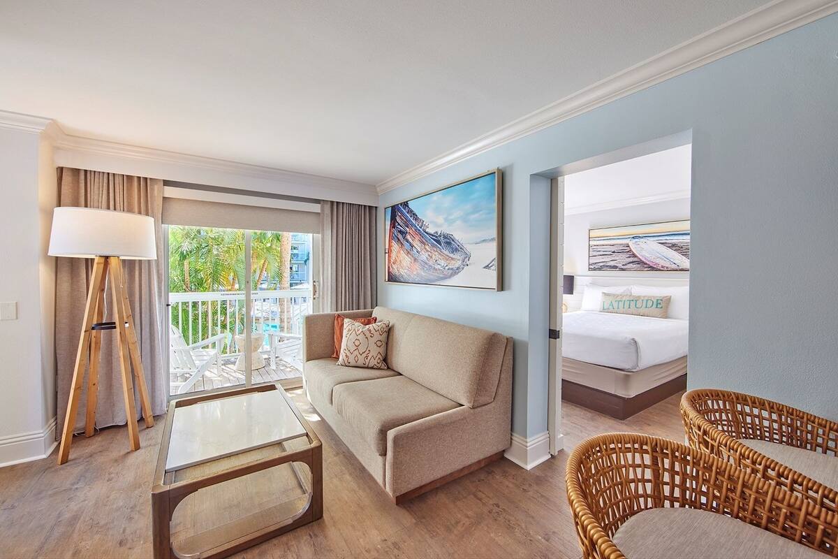 A hotel room with a balcony, a sofa, a coffee table, and wicker chairs.