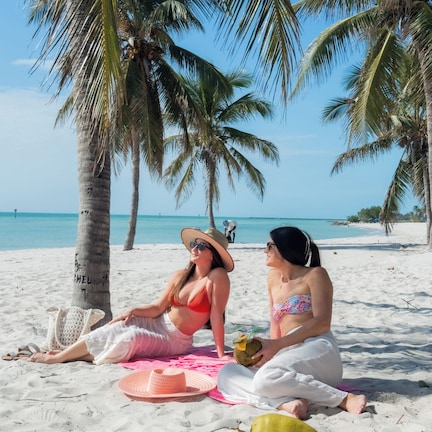 Two people sitting on a beach with palm trees and a clear sky.