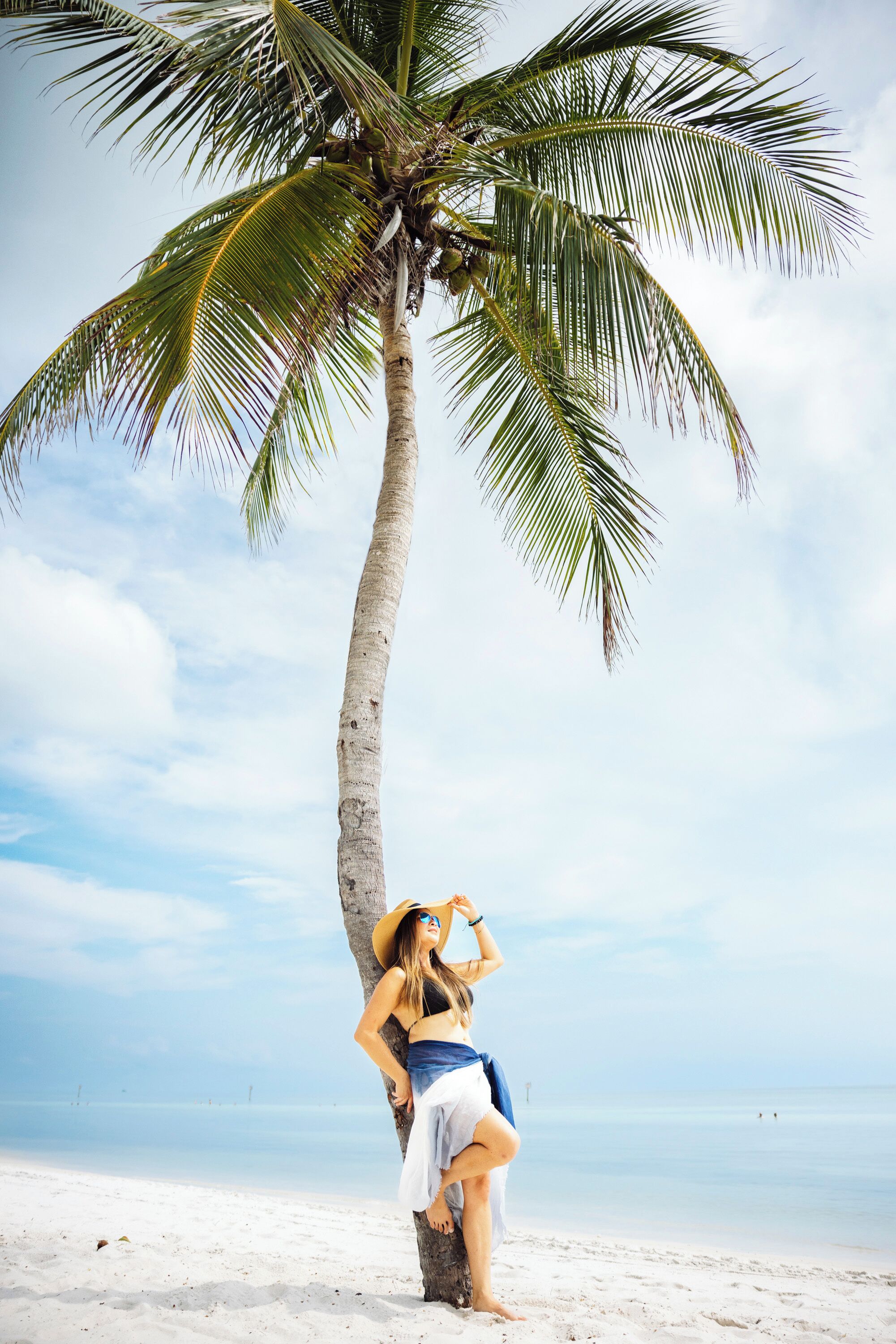 A person standing under a palm tree on a beach.