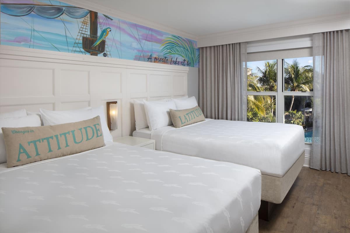 A hotel room with two beds, a mural on the wall, and a view of palm trees through the window.
