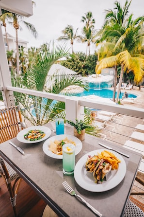 A dining table with plates of food, a drink, and a view of a pool and palm trees.