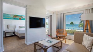 Habitación de hotel con cama, televisor, mesita de café, sofá y vista al océano.