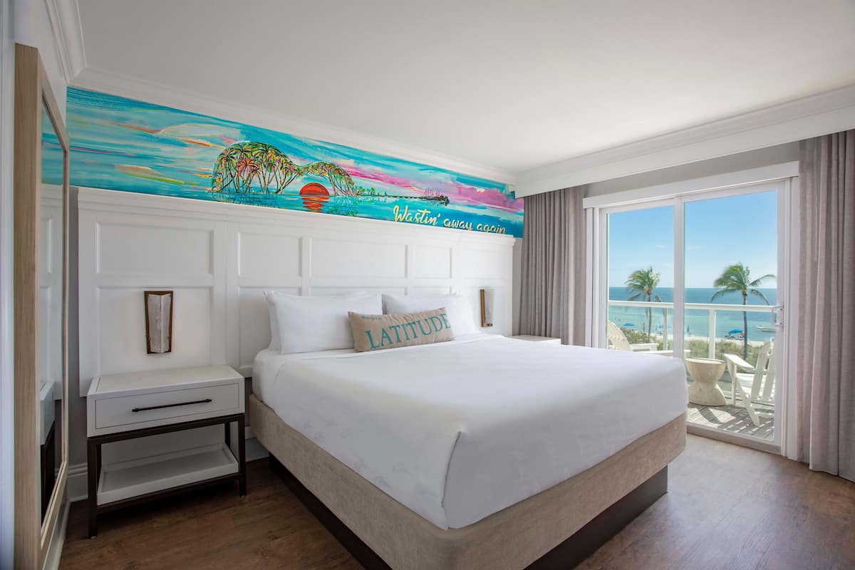 A large bed with white linens, a nightstand, and a painting above it.