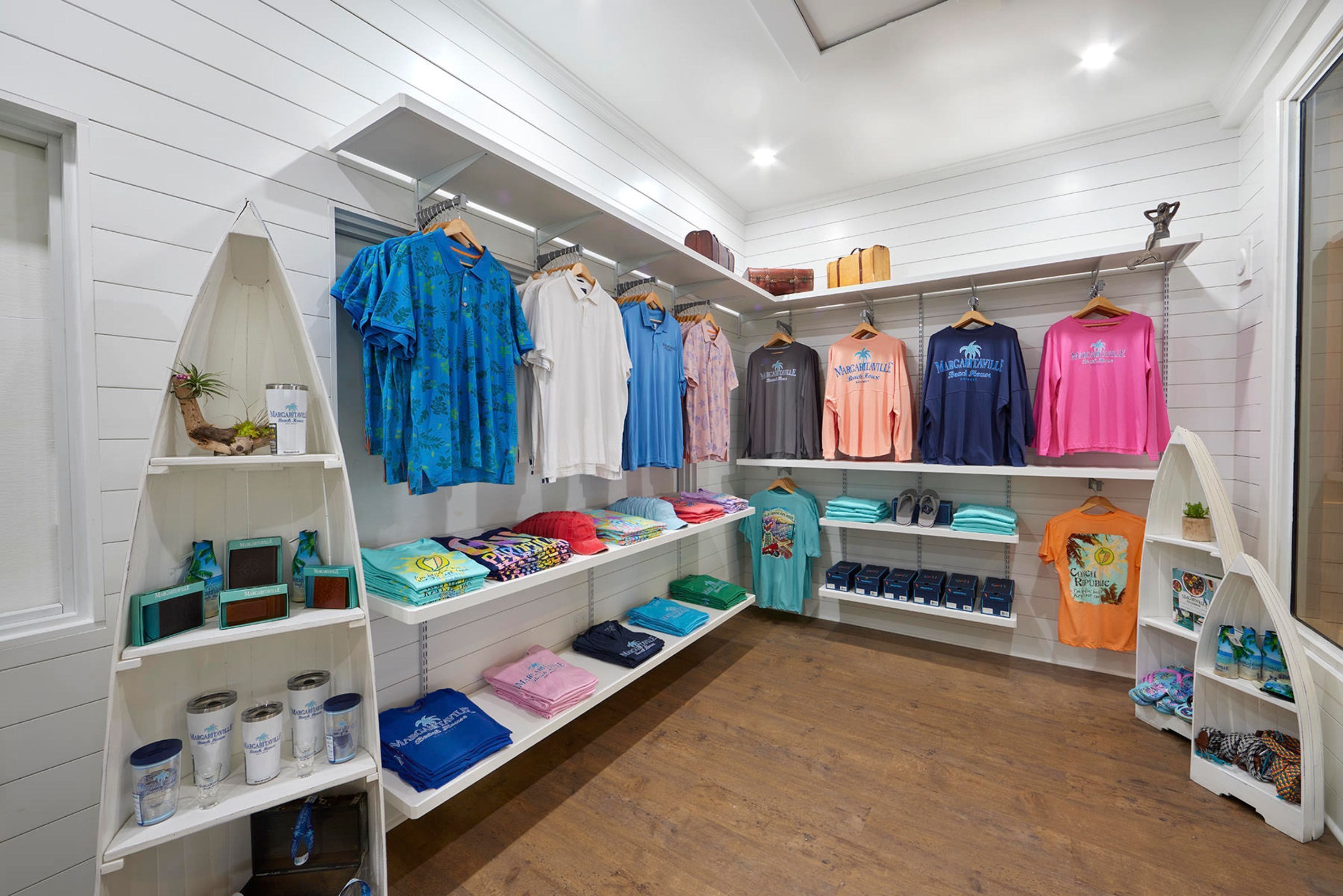 Un magasin de vêtements avec des étagères remplies de chemises et de pantalons, un présentoir de chaussures et une petite plante posée sur une étagère.