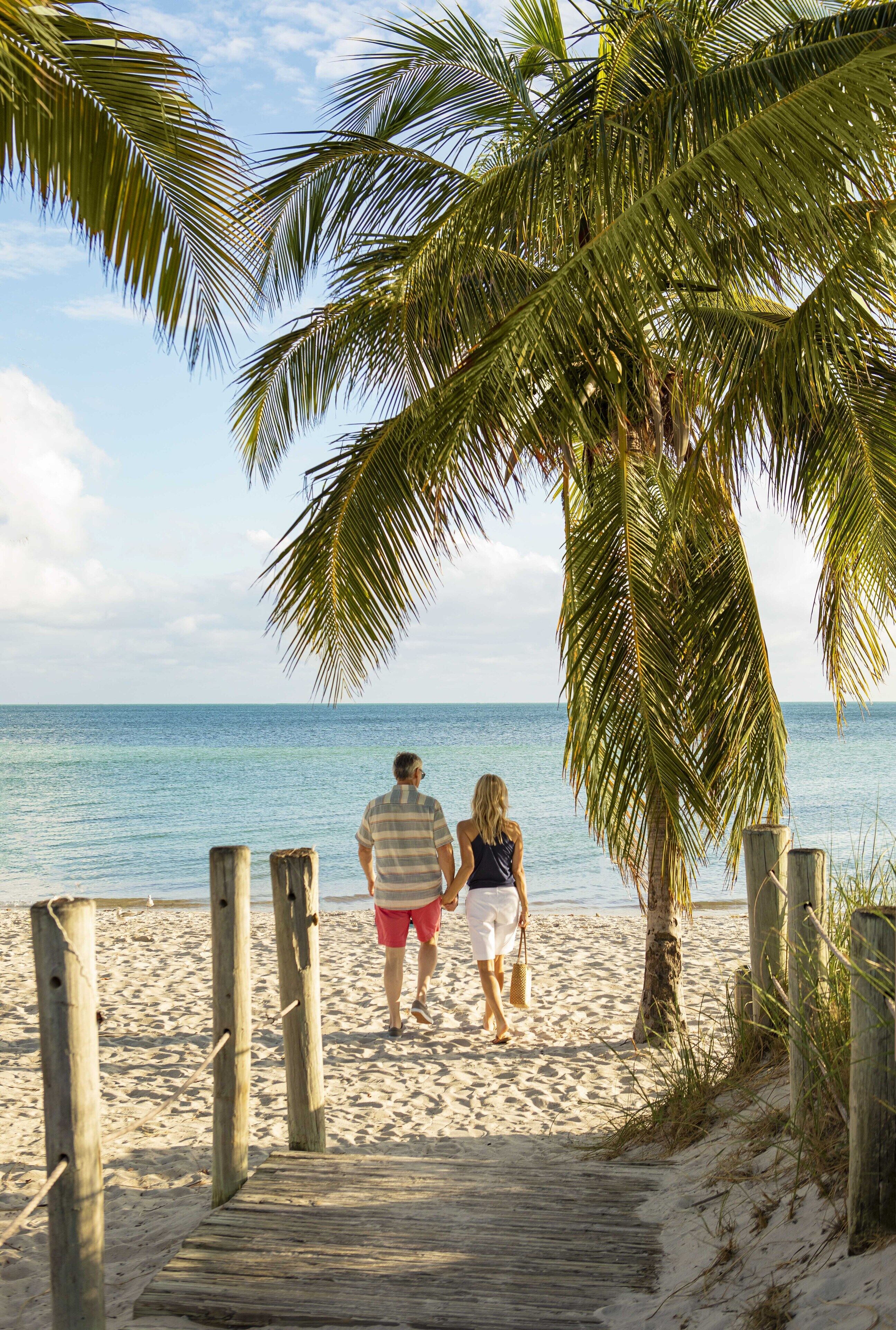 A wooden boardwalk leading to a beach with palm trees and a clear view of the ocean.