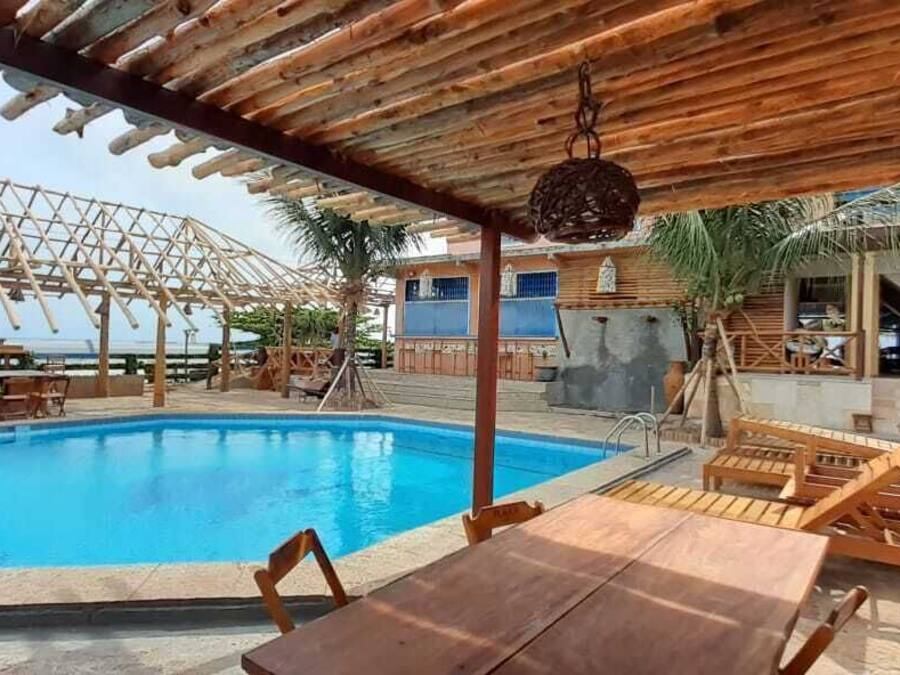 Un área de piscina con pérgolas de madera, sillones de descanso y una mesa.