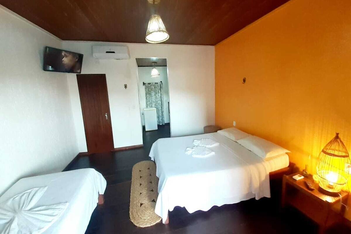 A room with two single beds, a small table, a lamp, and a television on the wall.