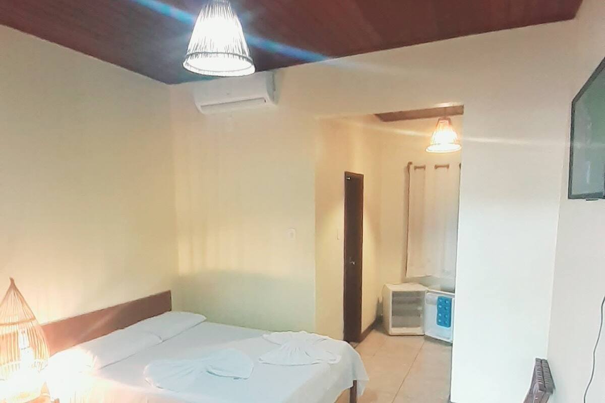A hotel room with two beds, a wooden ceiling, a tiled floor, and a small table with a lamp.