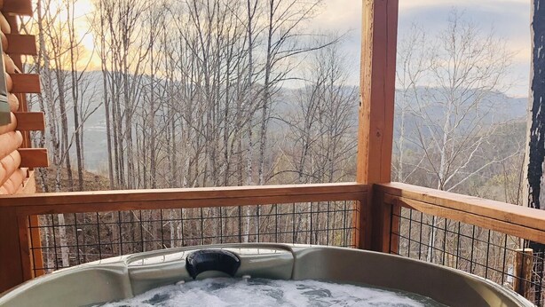 Een hottub op een houten terras met uitzicht op bomen en bergen.