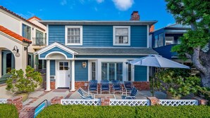 A two-story house with a blue exterior, a front porch with chairs, and a small pool.