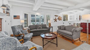 A spacious living room with a fireplace, two sofas, a coffee table, and a large window with blinds.