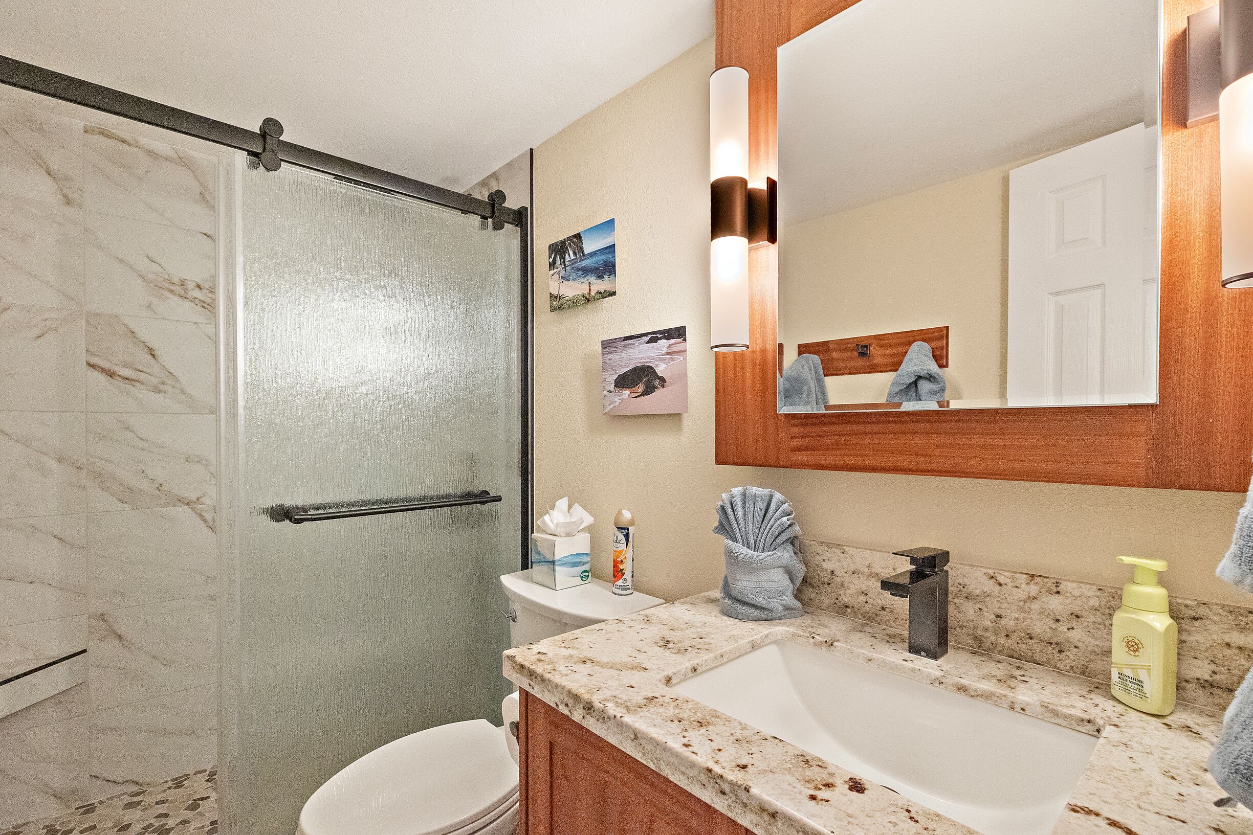 A bathroom with a shower, toilet, sink, and a large mirror.