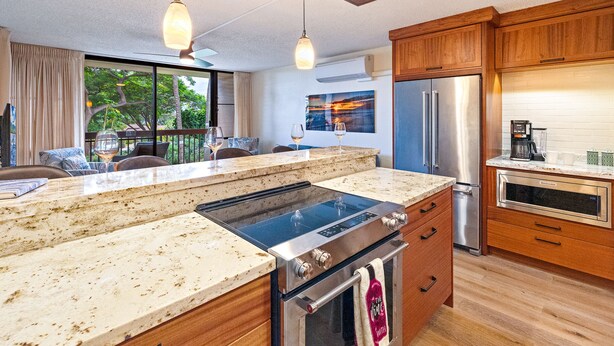 A modern kitchen with a large island, stainless steel appliances, wooden cabinets, and a view of the outdoors. - Totally Renovated Maui paradise condo steps away from the beaches of South Kihei (Kihei)