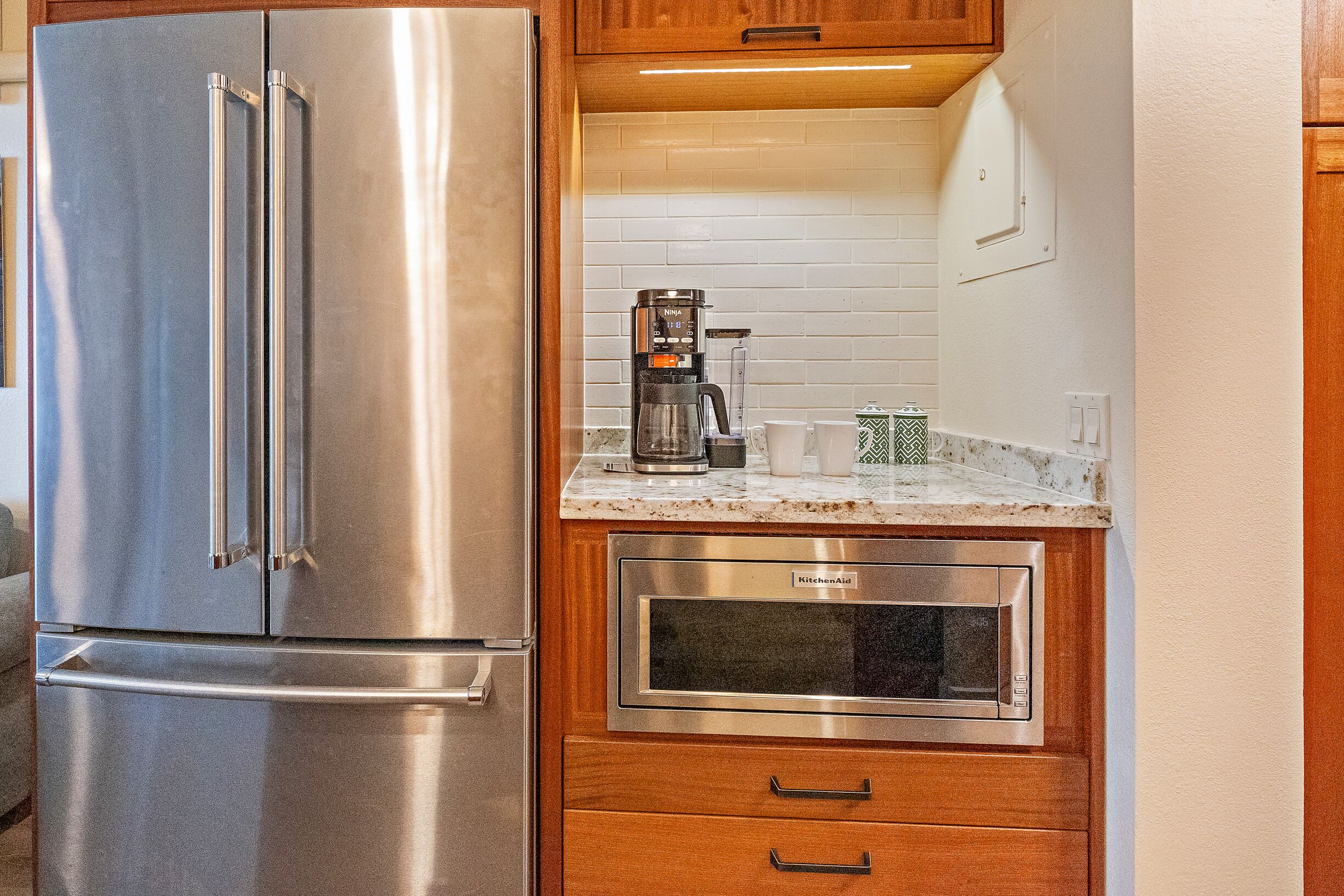 Una cocina con un refrigerador de acero inoxidable, una cafetera y un microondas integrado.