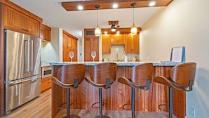 A kitchen with wooden cabinets, stainless steel appliances, and bar stools. - Totally Renovated Maui paradise condo steps away from the beaches of South Kihei (Kihei)