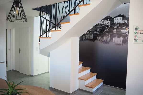 A modern staircase with wooden steps and black metal railings, leading to a room with a large black and white mural of a waterfront scene.