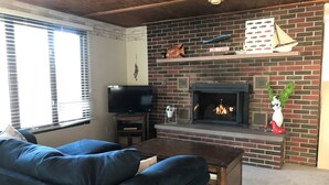 A living room with a brick fireplace, a television, and a large blue sofa. - Beautiful Skinner Cottage overlooking the lake (Albion)