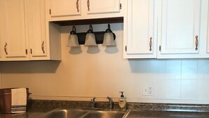 A kitchen with white cabinets, a granite countertop, a double sink, and three wall-mounted lights. - Beautiful Skinner Cottage overlooking the lake (Albion)