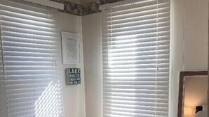 A room with two windows, a bed, a small table, and a mirror. - Beautiful Skinner Cottage overlooking the lake (Albion)