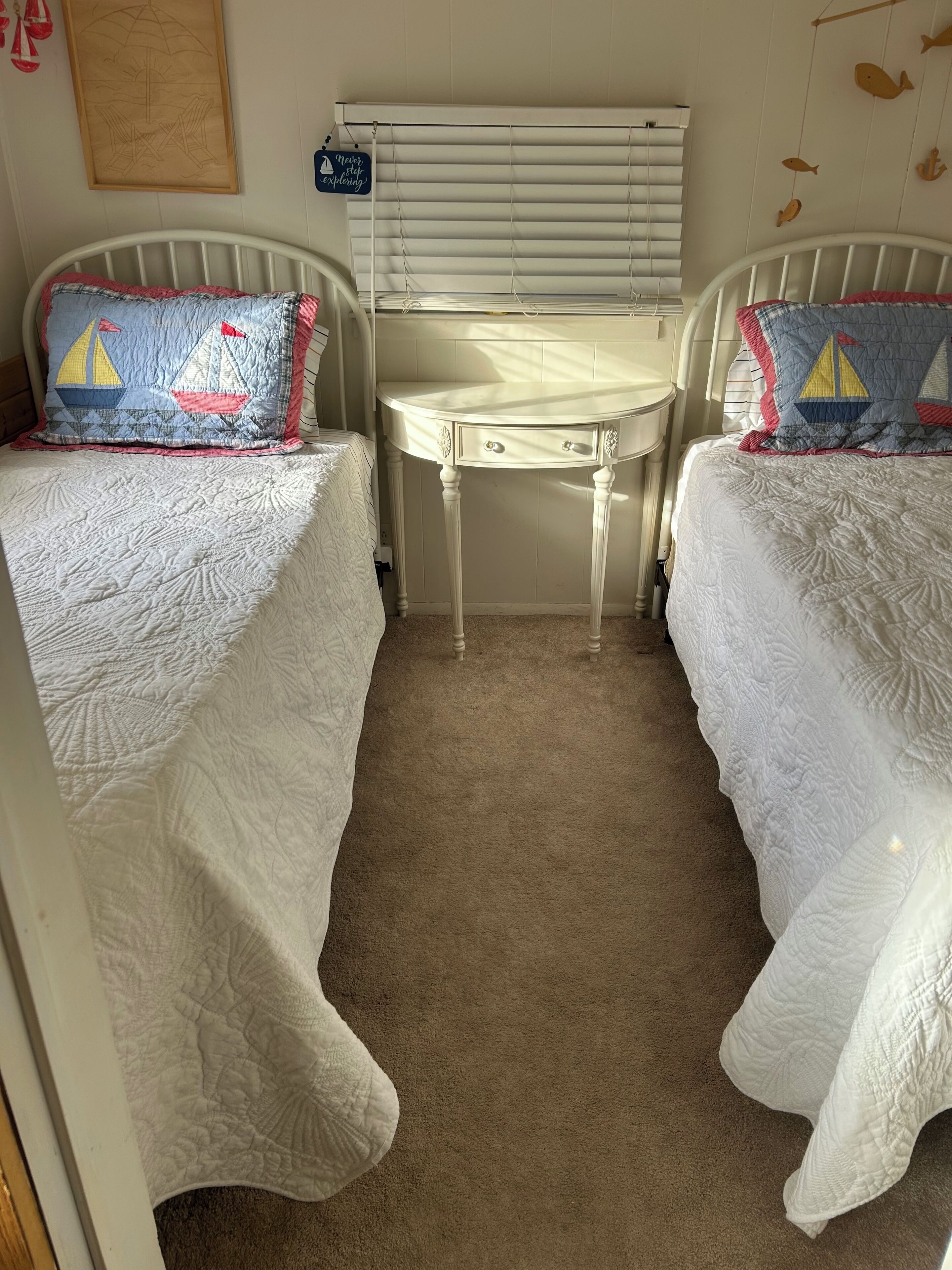 Un dormitorio con dos camas, una mesita blanca y una ventana con persianas.