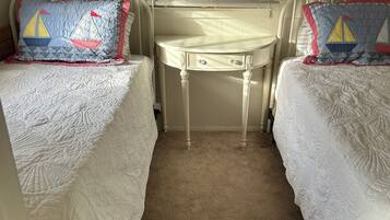 Un dormitorio con dos camas, una mesita blanca y una ventana con persianas.