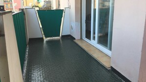 En smal korridor med en grön dörr, ett kaklat golv och en glasdörr som leder ut till ett utomhusområde.