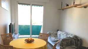 Ett mysigt rum med ett runt, gult bord, flätade stolar, en soffa med blommönster och en liten hylla med dekorativa föremål.