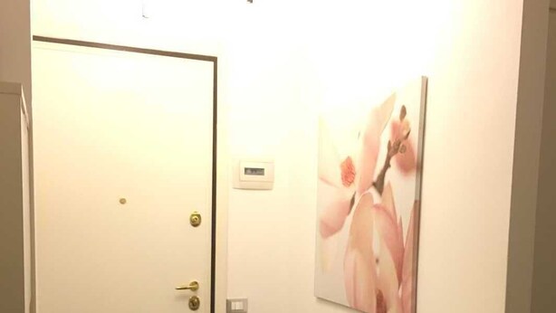 En hall med trägolv, en vit dörr med ett mässingshandtag och en väggmonterad termostat.