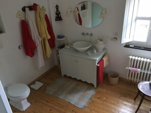 A bathroom with a white sink, mirror, and toilet. There are towels and a rug on the floor.