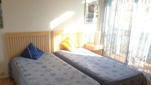 A room with two beds, each with a patterned bedspread, a wooden headboard, a nightstand with a lamp, and a window with curtains.
