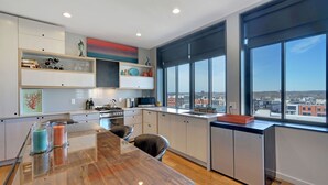 Een moderne keuken met een groot schiereiland, veel daglicht en uitzicht over de stad door grote ramen.
