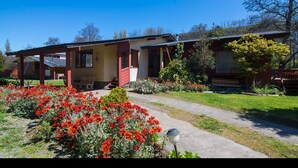 A two-story house with a covered porch, a front yard with red flowers, and a small garden area. - Cabañas Terrazas del Lago (Puerto Varas)