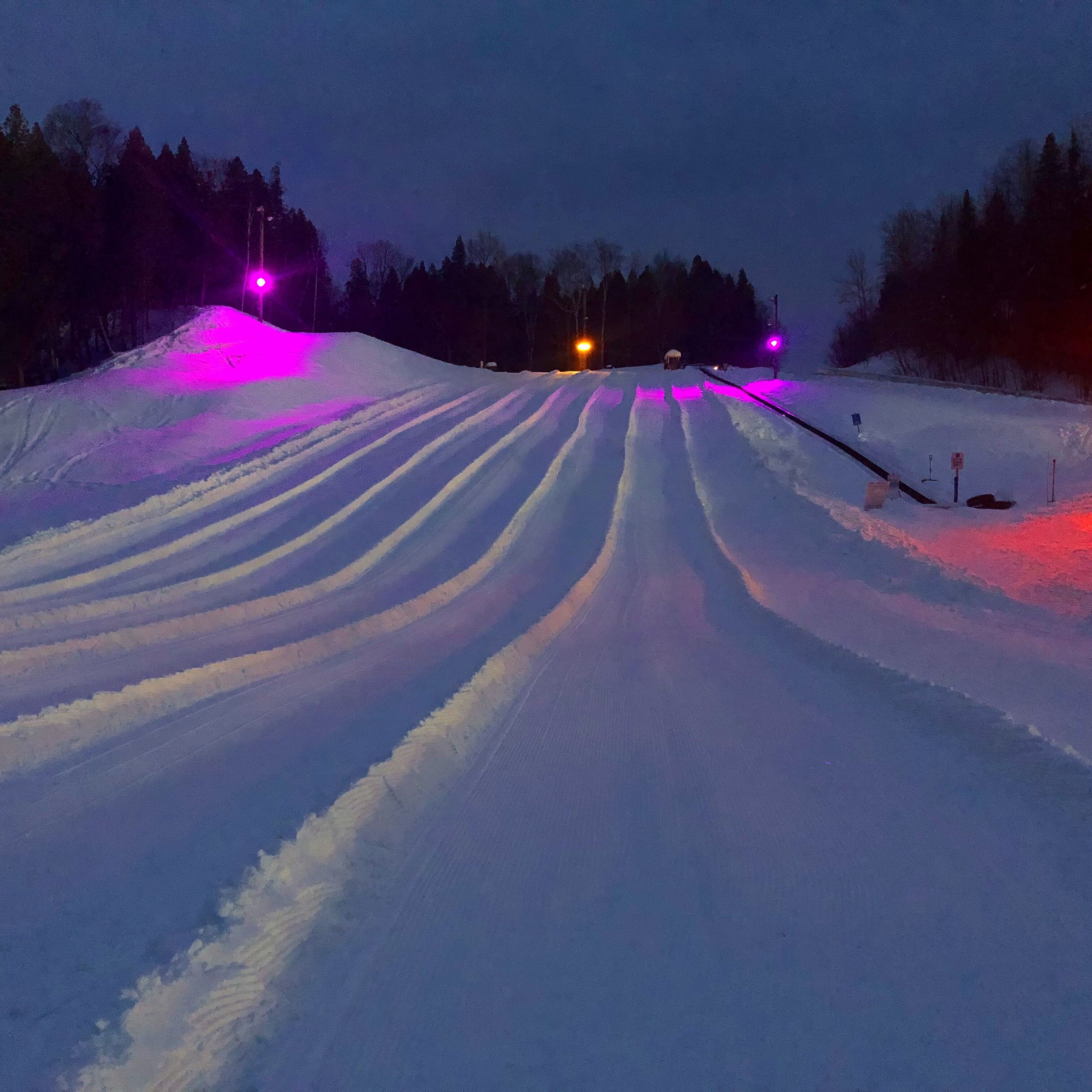 A snowy road with tire tracks and a few vehicles.