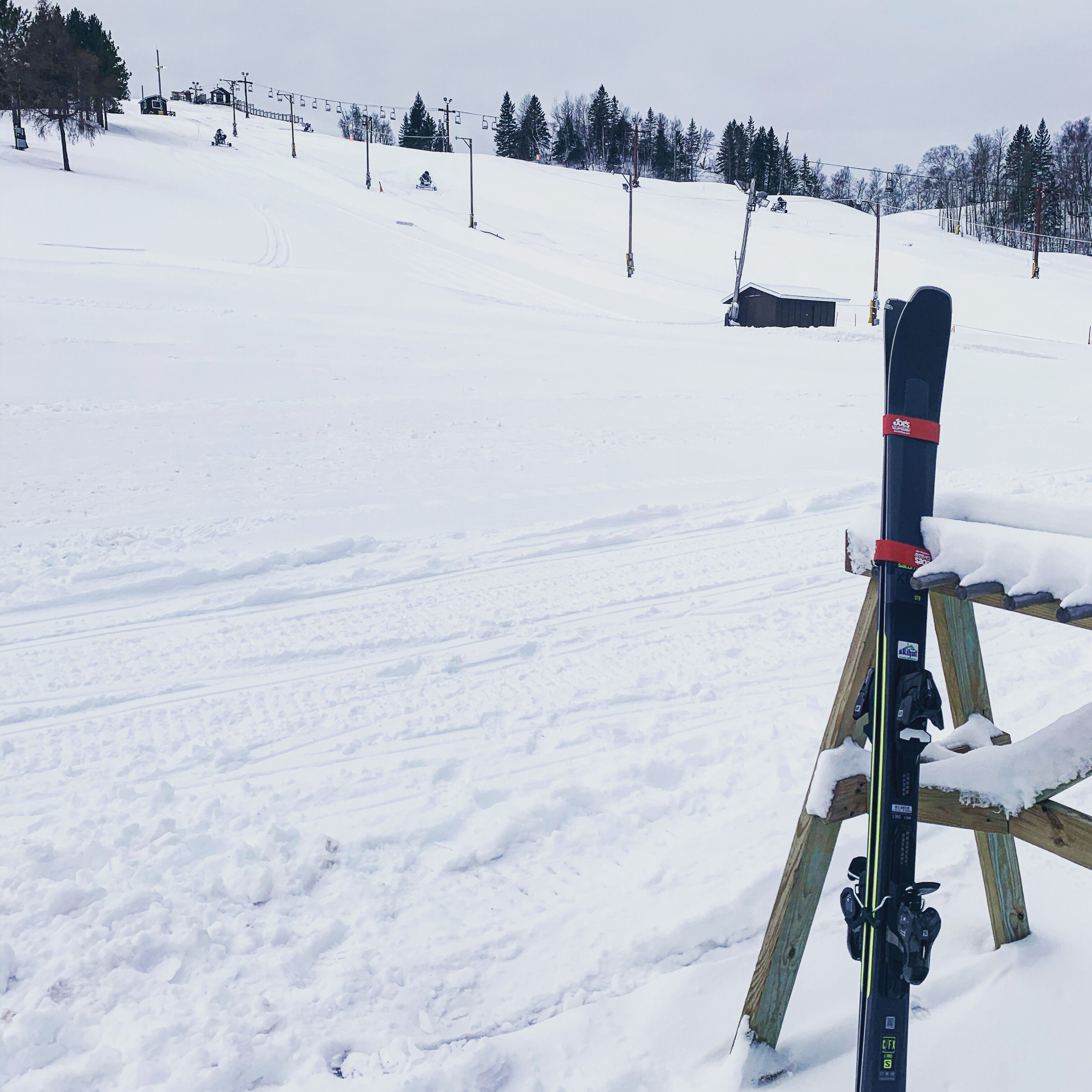 A ski lift chair with skis leaning against a wooden post, set against a snowy mountain slope.
