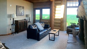 A log cabin interior with a leather sofa, a coffee table, and a view of a forest through large windows. - Mont du Lac Resort (Superior)