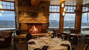 A dining area with a stone fireplace, round tables set for four, and a view of the landscape through large windows. - Mont du Lac Resort (Superior)