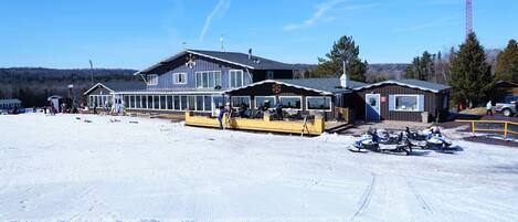 A snow-covered area with a building that has a large window and a covered outdoor seating area.