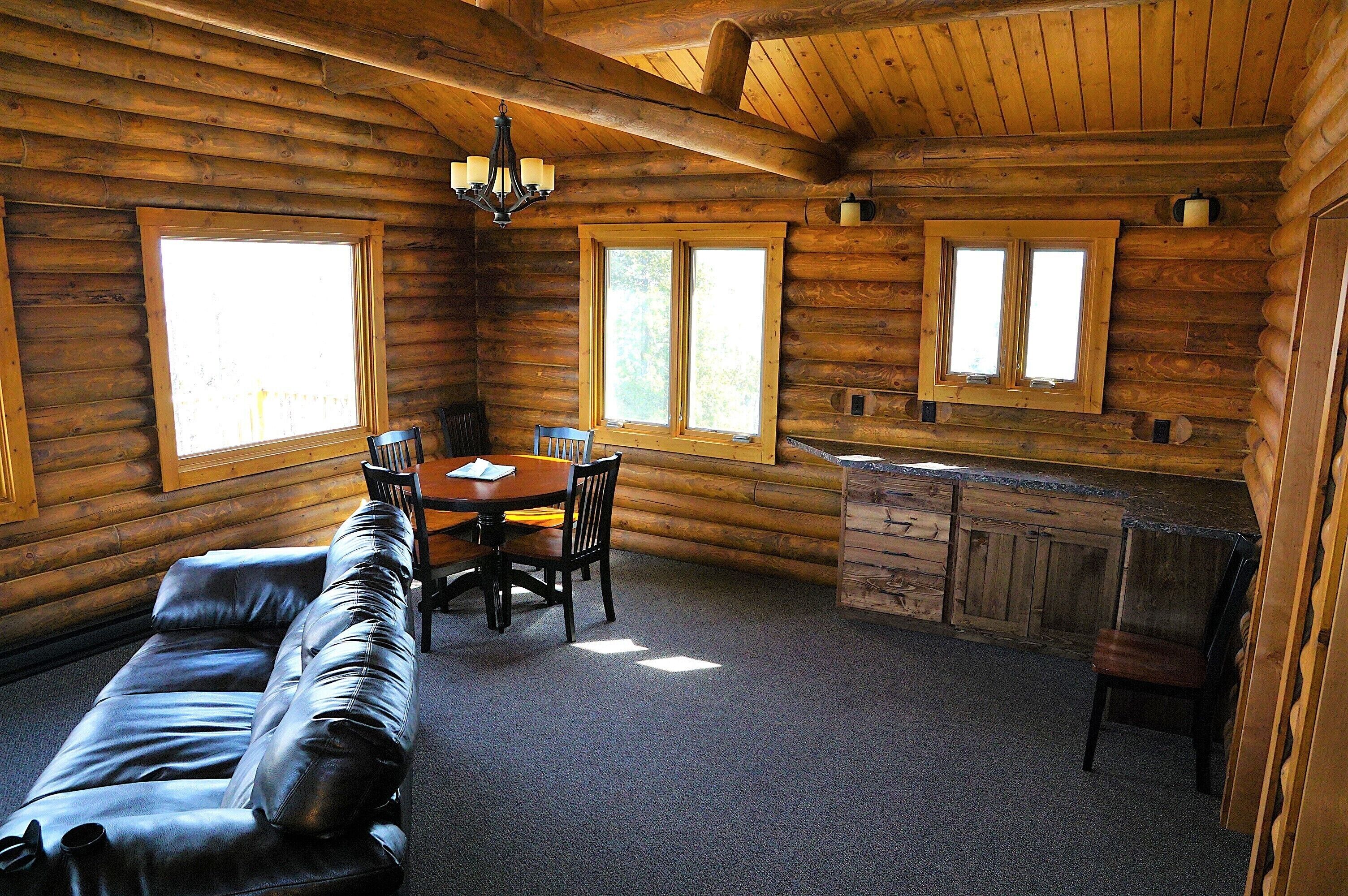 Interior de una cabaña de troncos con comedor, sofá y cocina.
