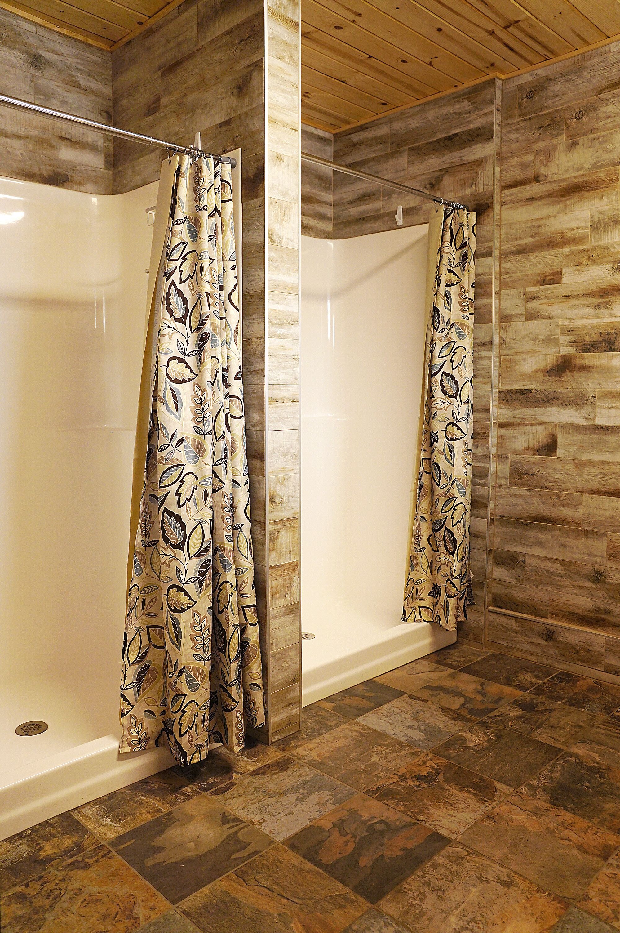 A shower area with a patterned shower curtain, a white bathtub, and a wooden floor.