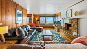 A cozy living room with a fireplace, wooden walls, a sofa, and a view of the ocean. - Waterfront property + Beach + Internet (Sturgeon Bay)