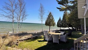 A patio with wicker furniture overlooking a body of water, surrounded by trees. - Waterfront property + Beach + Internet (Sturgeon Bay)