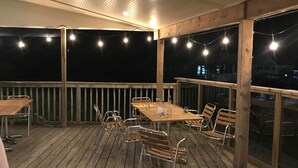 An outdoor deck with a wooden table and chairs, string lights, and a view of the city at night.