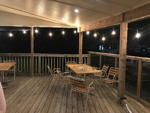 An outdoor deck with a wooden table and chairs, string lights, and a view of the city at night.