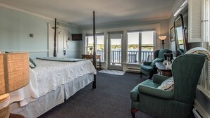 A bedroom with a bed, a chair, a desk, a television, and a balcony with a view.