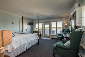 A bedroom with a bed, a chair, a desk, a television, and a balcony with a view.