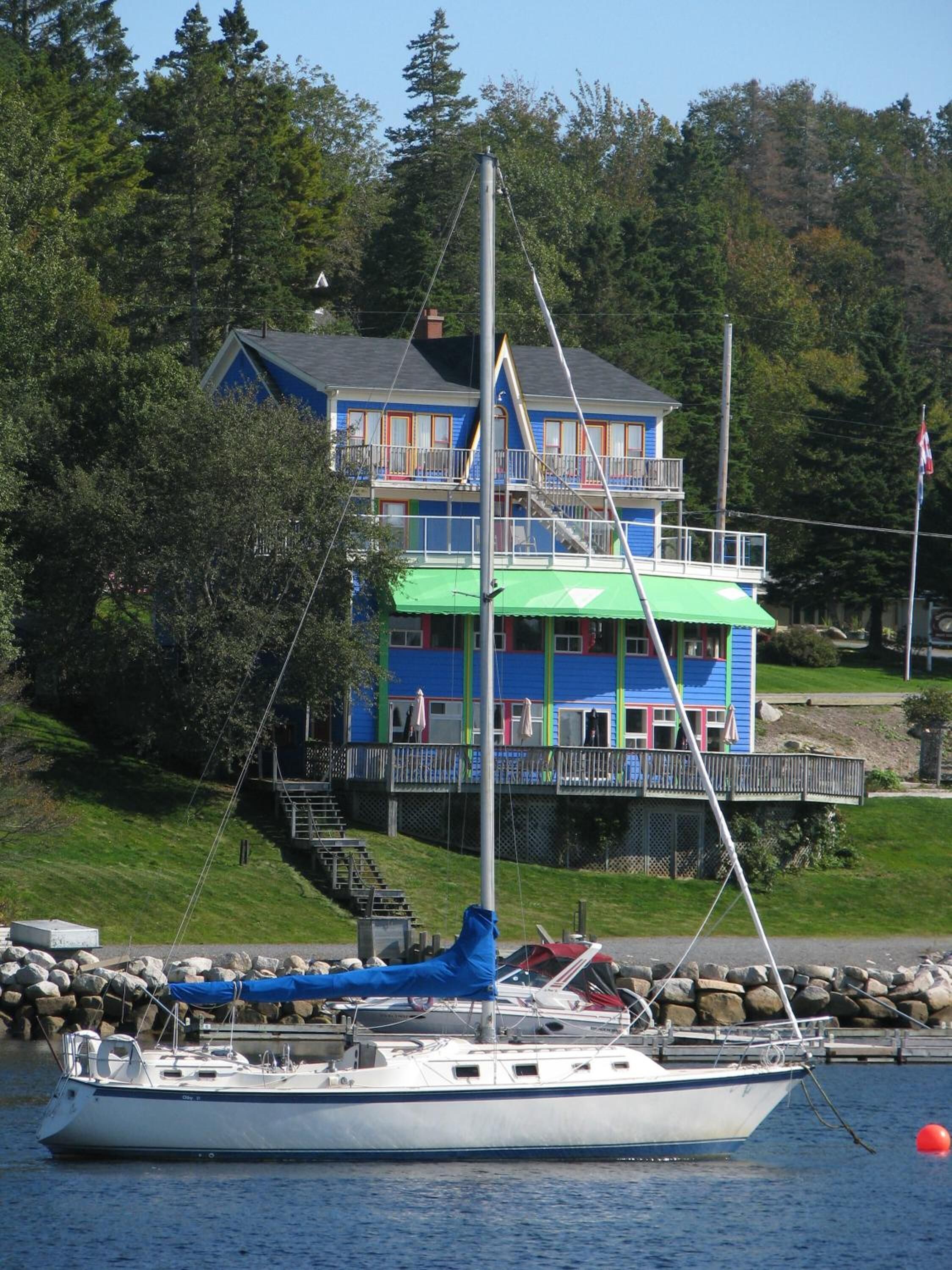 A sailboat docked near a two-story building with a green awning and a balcony.